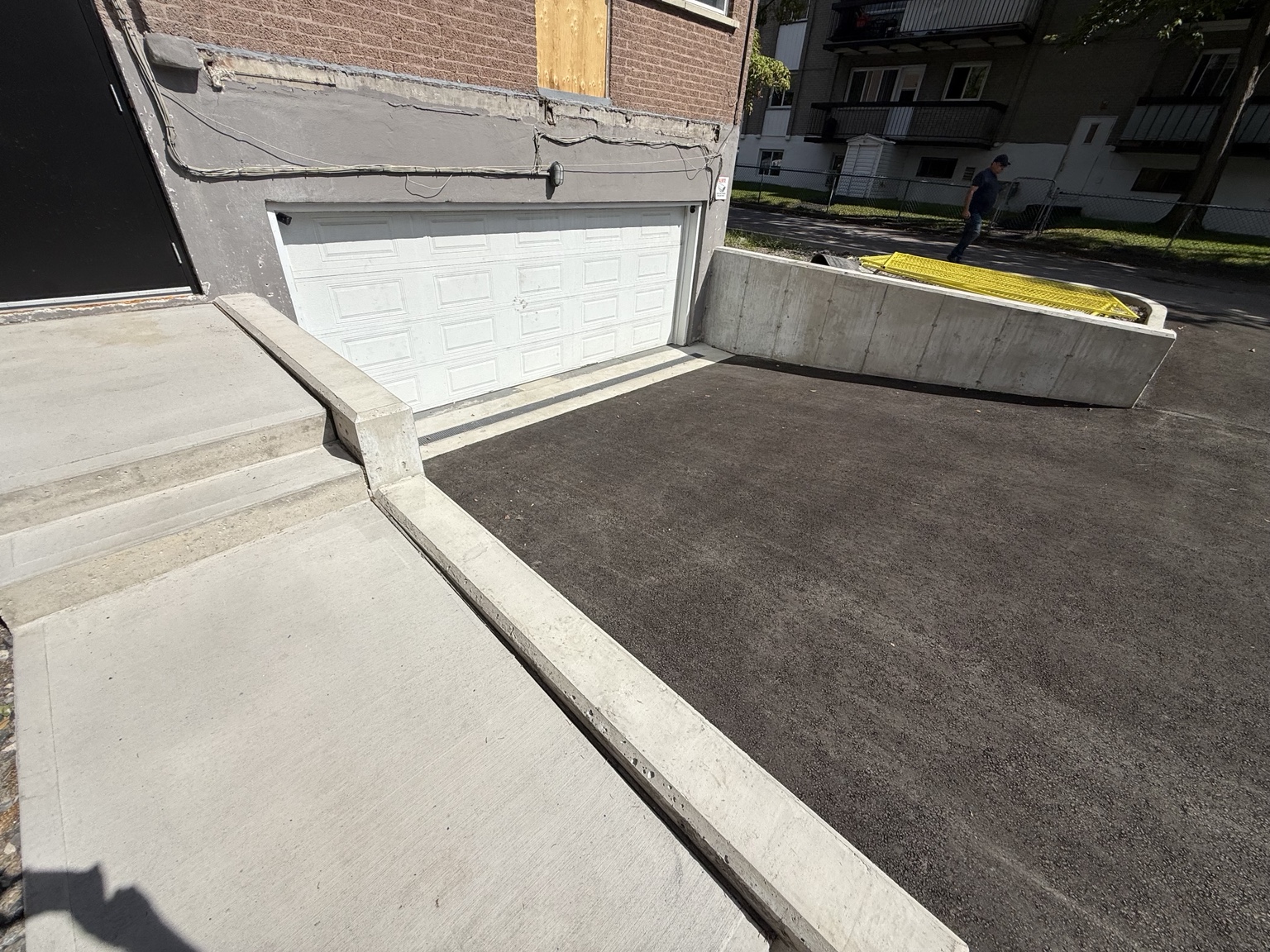 Mur de soutènement, escalier et trottoir en béton près d’un caniveau devant un garage à Rivière-des-Prairies